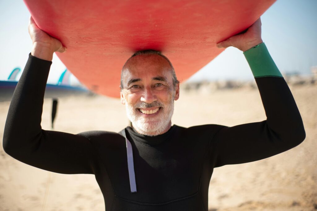 Smiling senior man holding a surfboard on a sunny beach in Portugal.