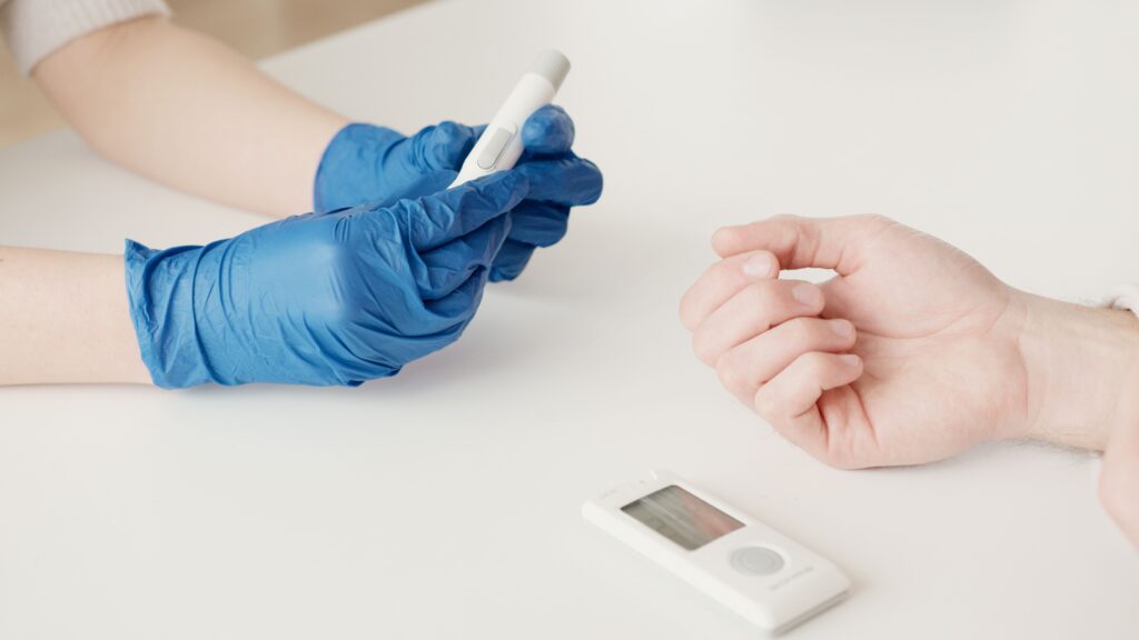 Gloved clinician preparing a lancet for a patient's finger-prick blood test, part of routine monitoring for people taking weight loss drugs.