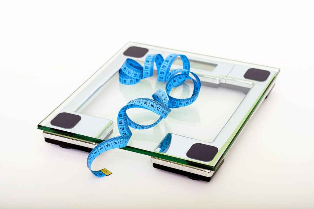 Digital glass bathroom scale with blue measuring tape, representing weight loss progress tracking and body measurement.