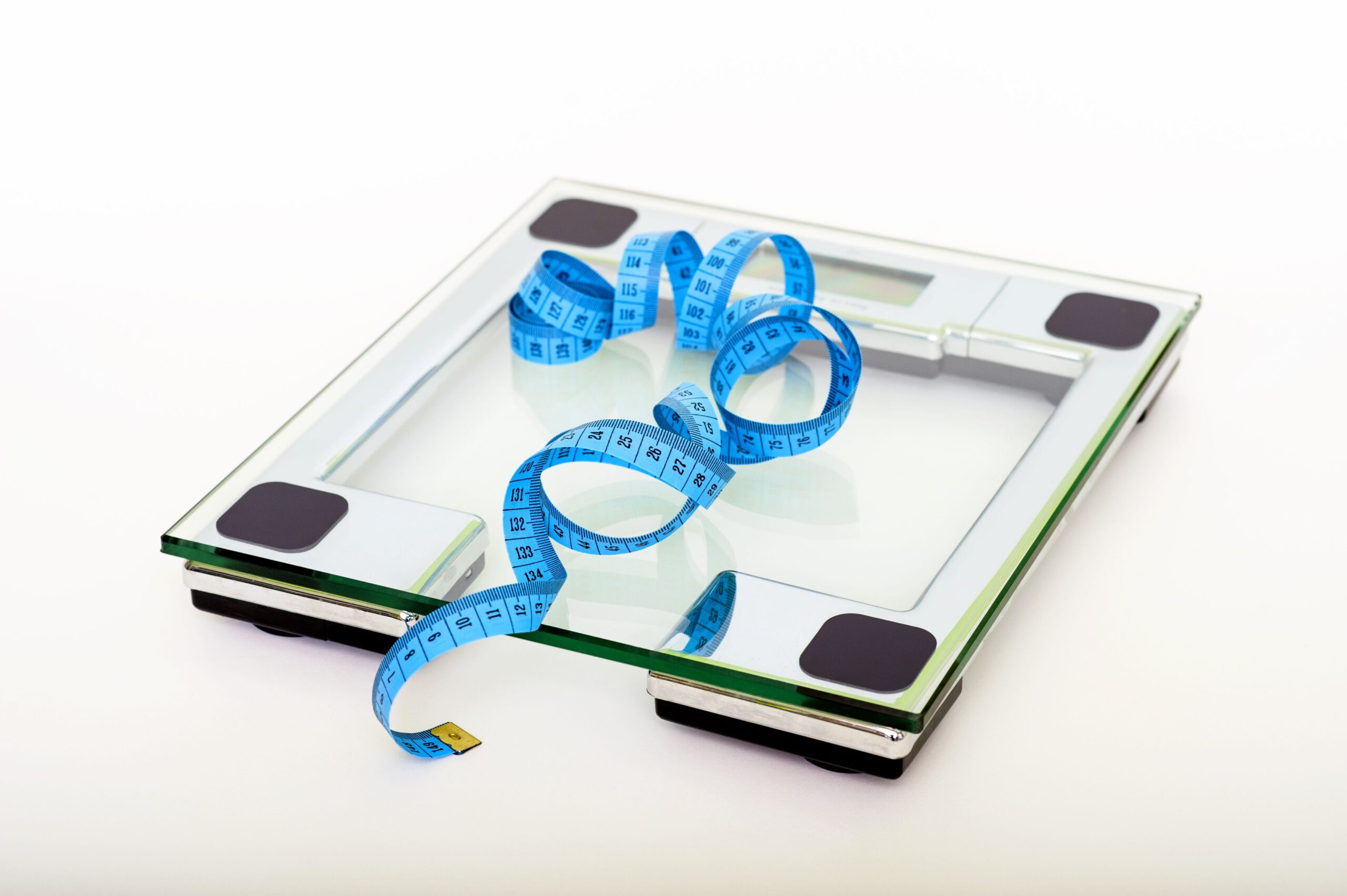Digital glass bathroom scale with blue measuring tape, representing weight loss progress tracking and body measurement.