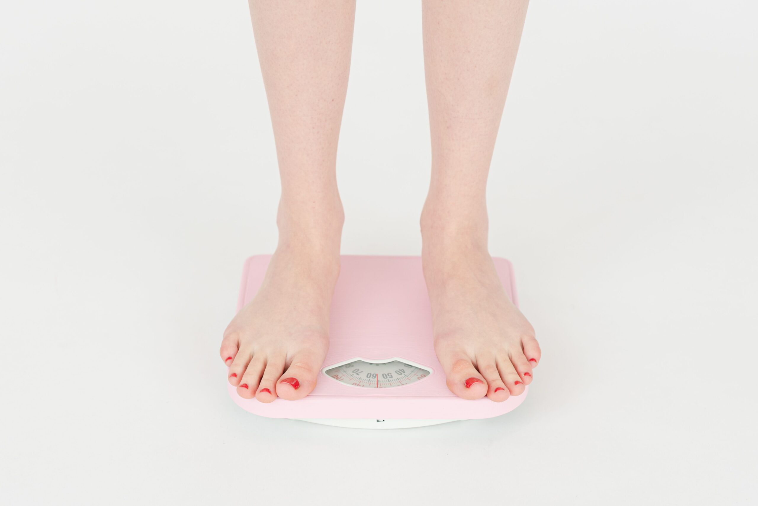 Person standing barefoot on a pink bathroom scale, checking weight during a medically supervised weight loss program.