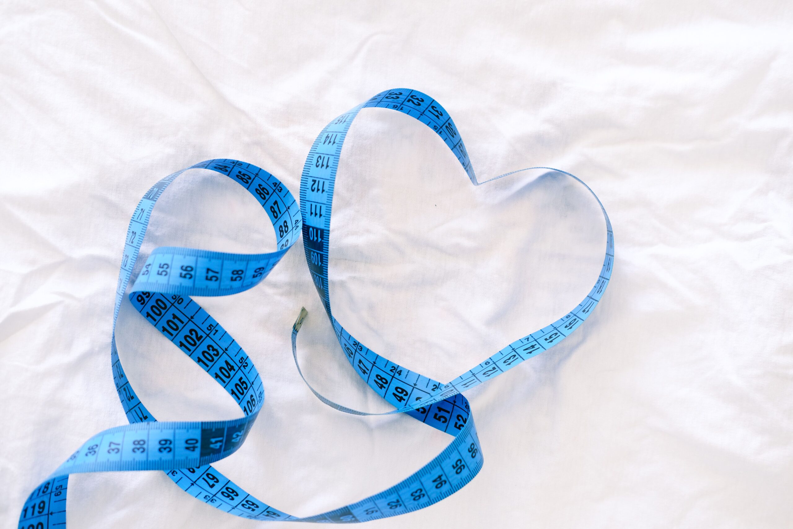 Blue measuring tape shaped into a heart, symbolizing heart health benefits of sustainable weight loss and lifestyle change.