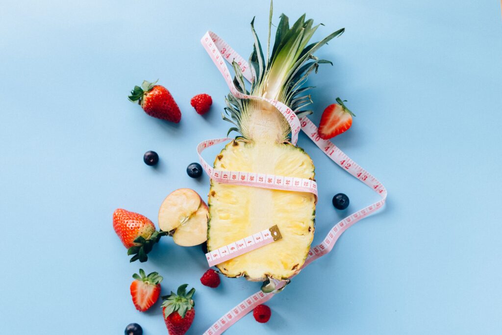 Halved pineapple with strawberries and blueberries encircled by a pink tape measure, illustrating a fruit-rich diet alongside weight loss medications.
