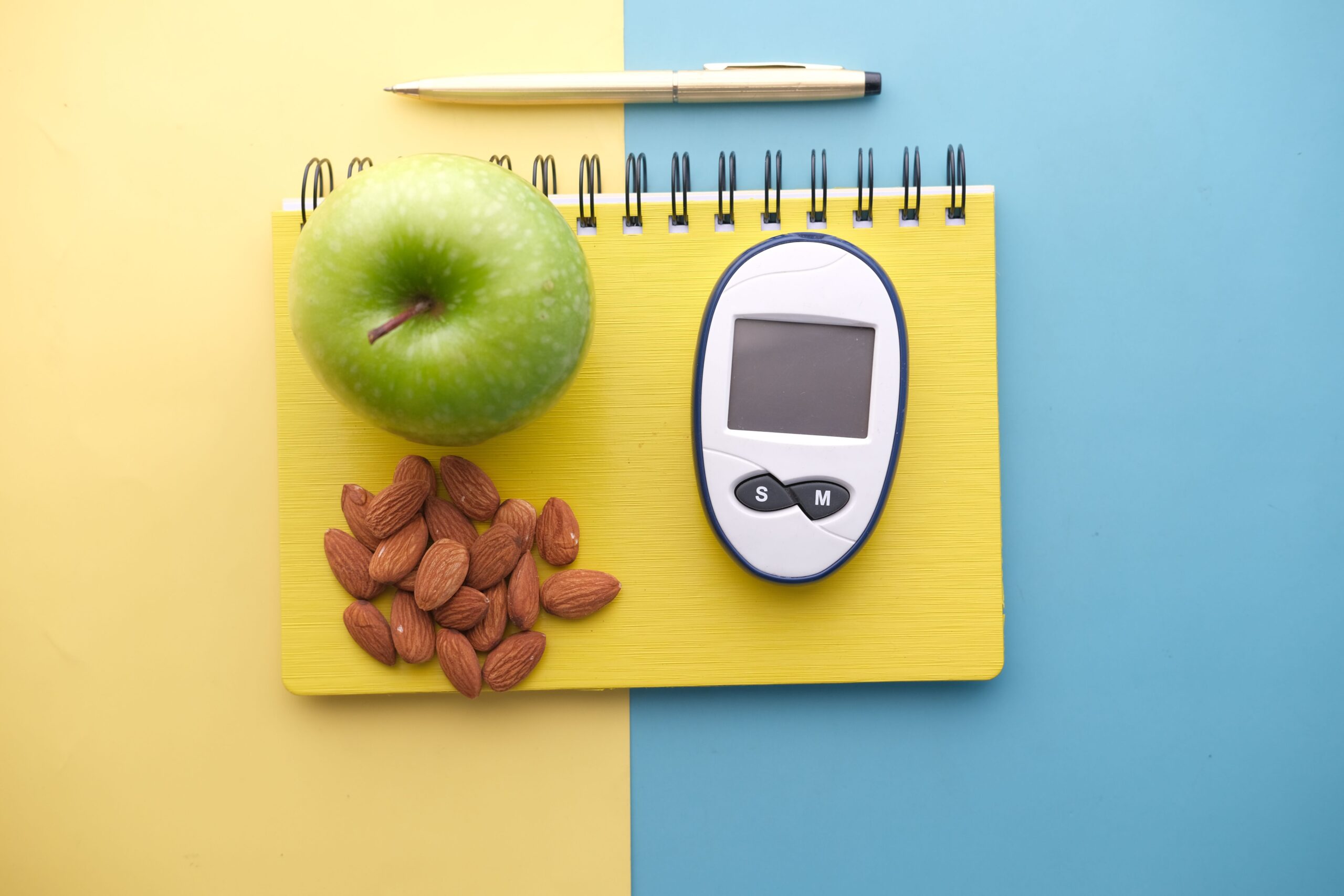 Green apple, almonds and a glucose meter resting on a yellow notepad, representing healthy snacking combined with weight loss supplements.