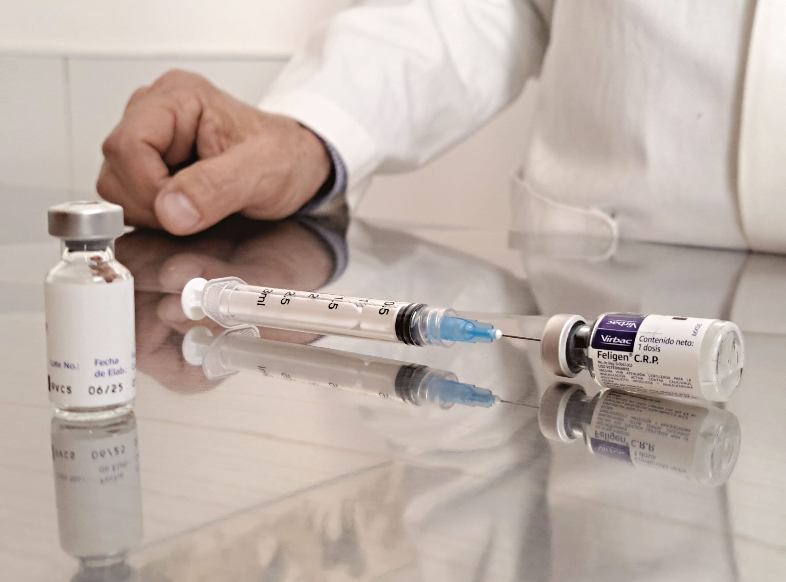 A clinician in a white coat draws weight loss medication from a small glass vial into a 3ml syringe on a reflective countertop.